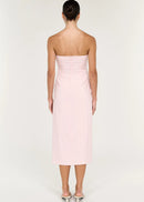 A woman modelling a pale pink strapless midi dress with gathered draping at the waist, photographed against a clean off-white studio background.
