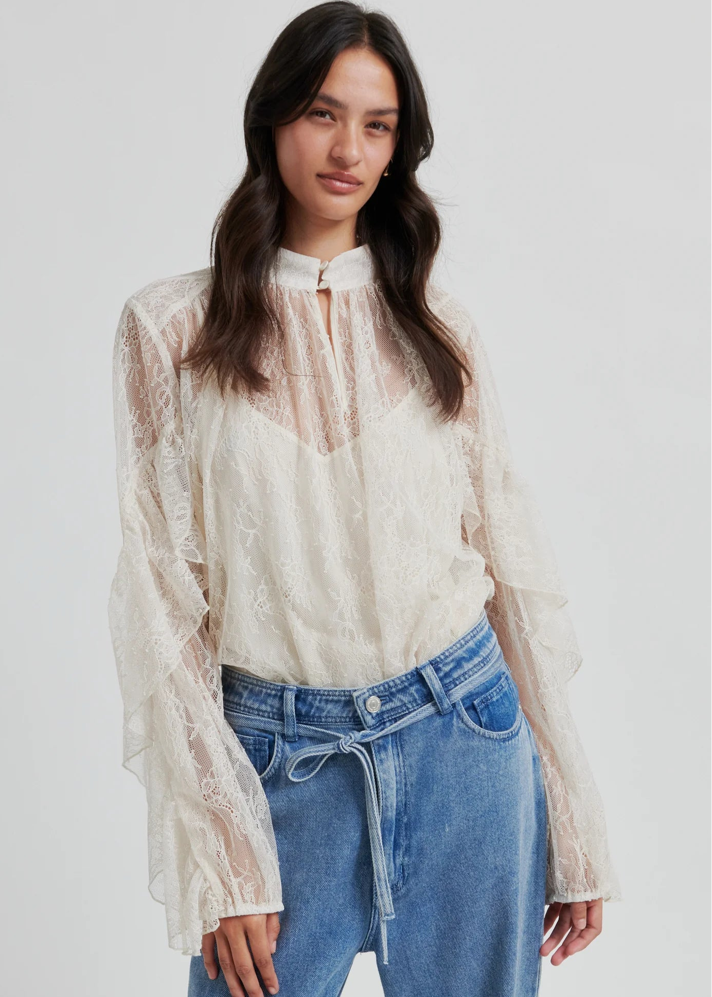 Woman wearing a lace blouse and blue jeans on a white background