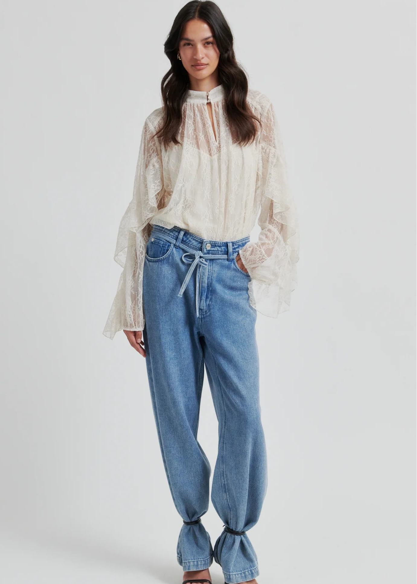 Woman wearing a lace blouse and blue jeans on a white background