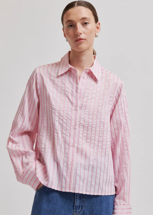 Woman wearing a pink  shirt with blue jeans on a light grey background