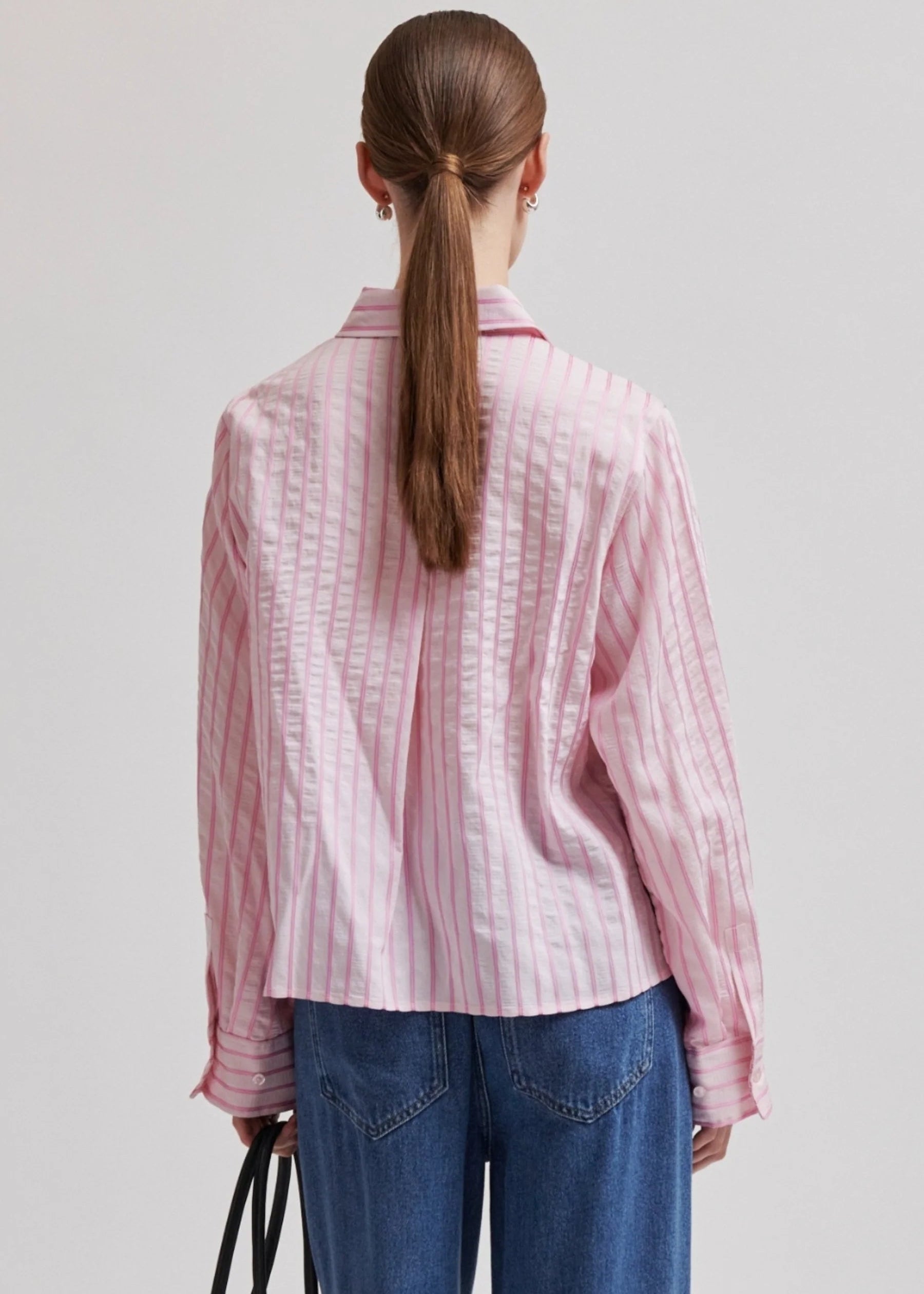 Woman wearing a pink  shirt with blue jeans on a light grey background