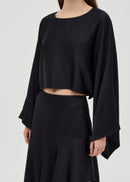 Person wearing a black outfit with a draped top and flowing skirt on a white background