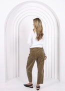 Woman wearing a white top and brown pants standing in a white archway.