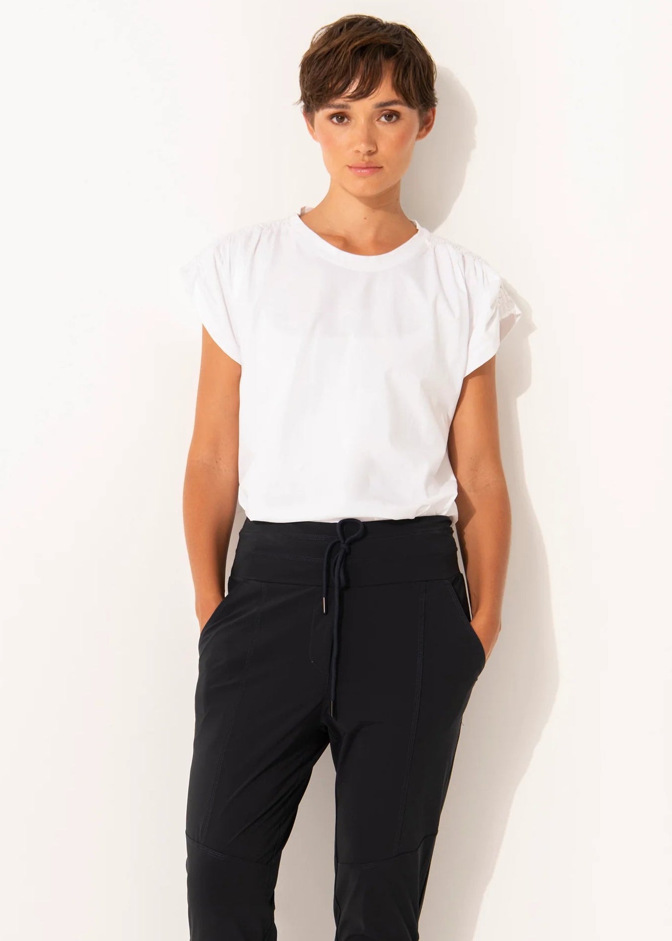 Woman wearing a white top and black pants against a white background