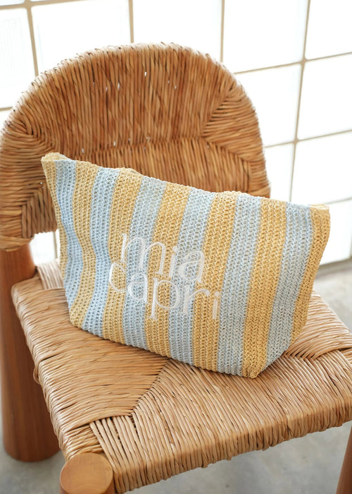 Striped bag with 'mia capri' branding on a wicker chair against a tiled wall.