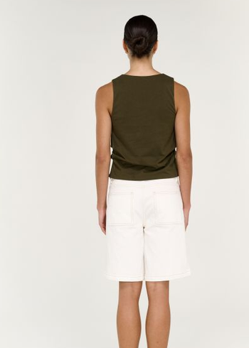 Woman wearing an olive green sleeveless top and white shorts on a white background