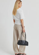 A woman modelling a white short-sleeve top with a draped, asymmetrical neckline and gathered front detail, paired with light beige drawstring pants, against a plain light grey studio background.