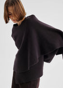 Person wearing a dark purple poncho against a white background
