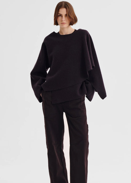 Person wearing a dark purple poncho against a white background