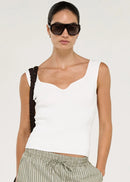 A model wearing a white ribbed knit scoop-neck tank top and green and white vertically striped trousers, accessorized with black sunglasses and a black woven shoulder bag, against a plain off-white background.