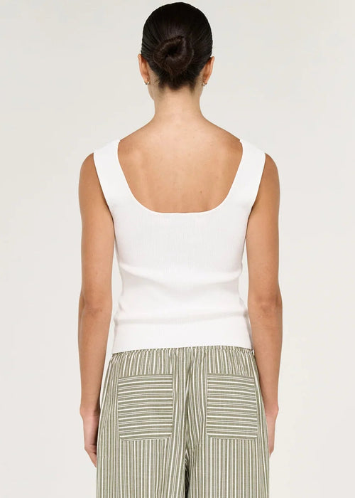 A woman viewed from the back wearing a white sleeveless top and wide-leg striped pants in a light sage green and white colourway, set against a plain off-white studio background.
