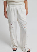 White pants with embroidered details worn by a person on a white background