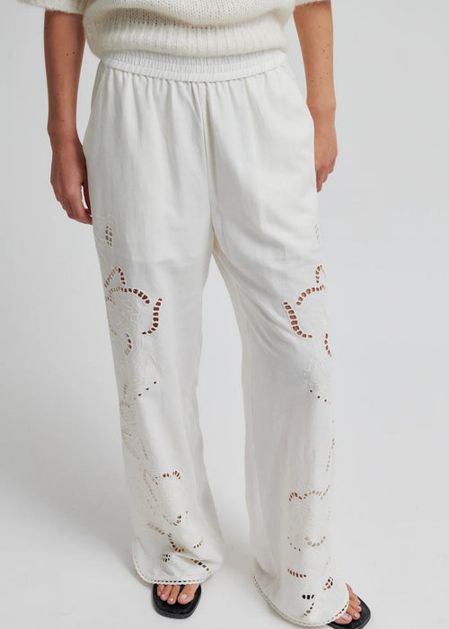 White pants with embroidered details worn by a person on a white background