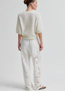 Woman wearing a white knit sweater and pants on a light grey background