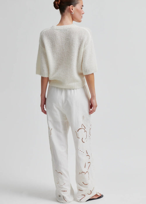 Woman wearing a white knit sweater and pants on a light grey background