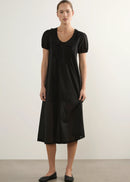 A woman modelling a black short-sleeve midi dress with a ruffled Peter Pan collar and gathered front, standing against a plain light grey studio background.
