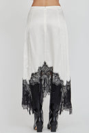 White skirt with black lace detailing worn with black boots on a white background