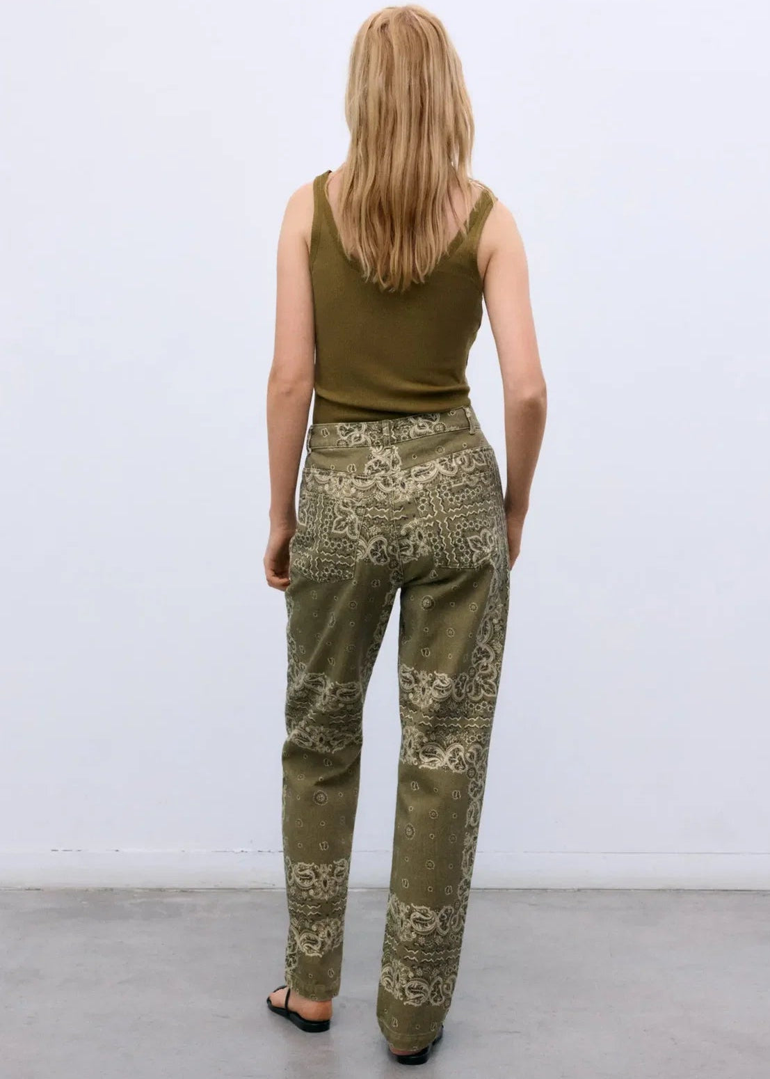 Woman wearing a green sleeveless top and patterned pants against a white background