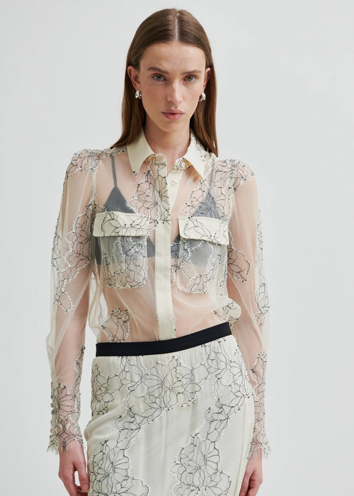 Model wearing a sheer blouse with floral embroidery against a white background
