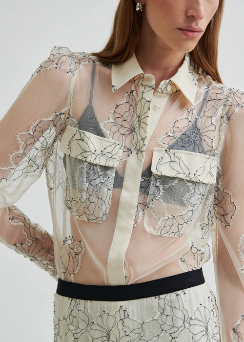 Model wearing a sheer blouse with floral embroidery against a white background