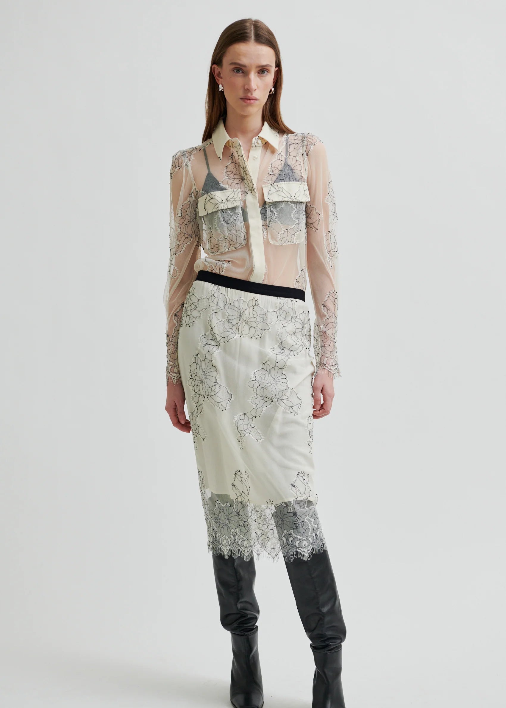 Model wearing a sheer blouse with floral embroidery against a white background