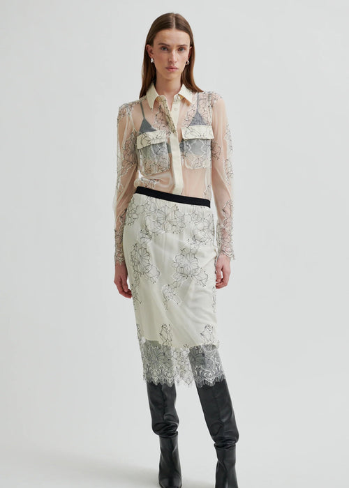 Model wearing a sheer blouse with floral embroidery against a white background