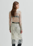 Model wearing a sheer blouse with floral embroidery against a white background
