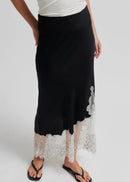 A black midi skirt with a sheer white lace hem and floral applique, worn by a model with a white top and black flip-flops against a light grey studio background.