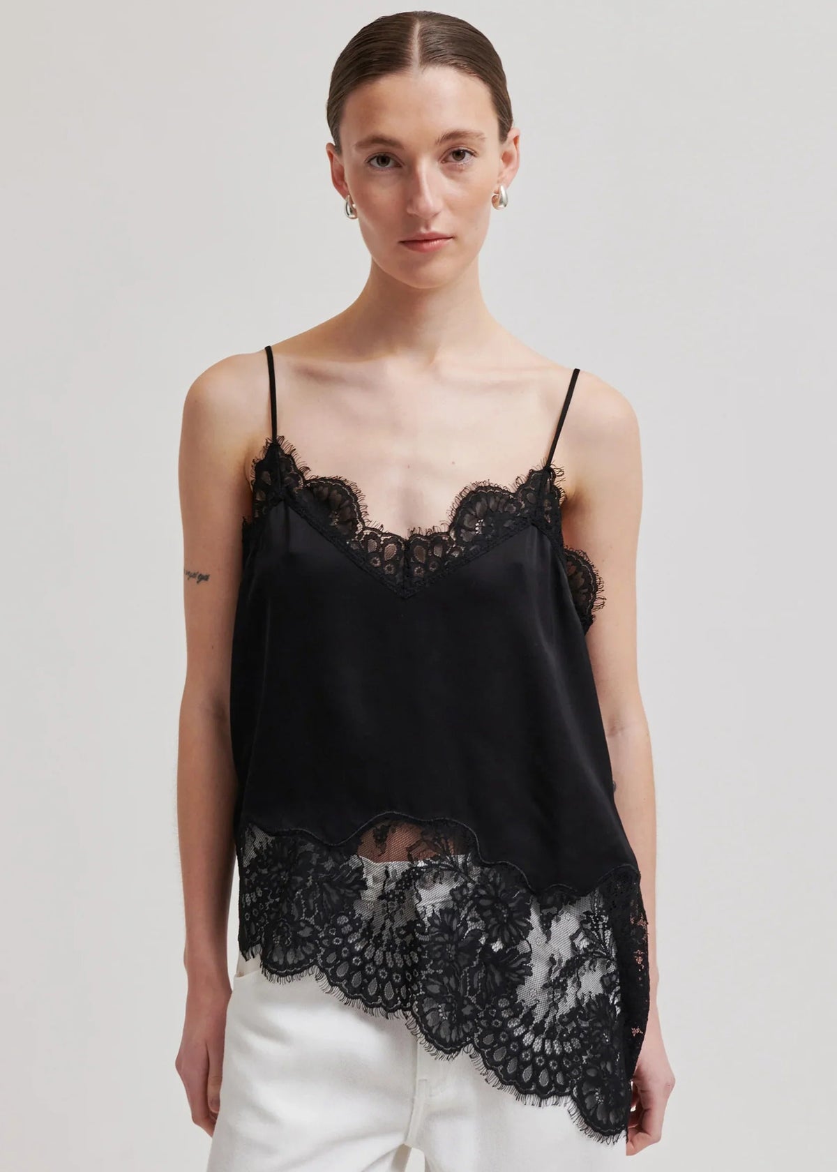 Woman wearing a black lace top and white pants on a plain background